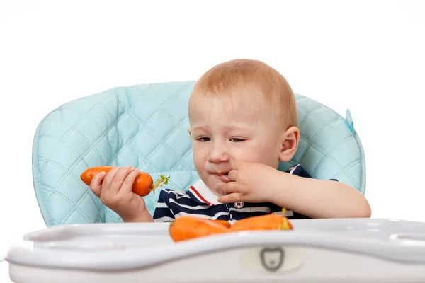 Веселый Маленький Мальчик Сидит Детском Кресле Ест Морковку Белом Фоне — стоковое фото