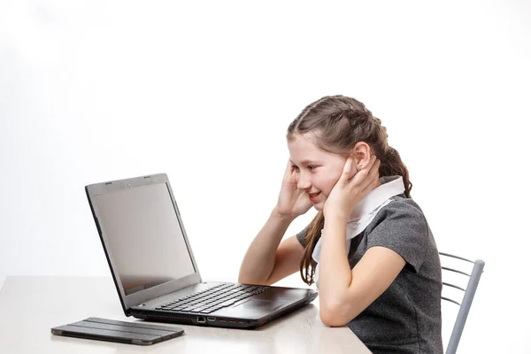 Söt skolflicka sitter vid en bärbar dator på en vit bakgrund — Stockfoto