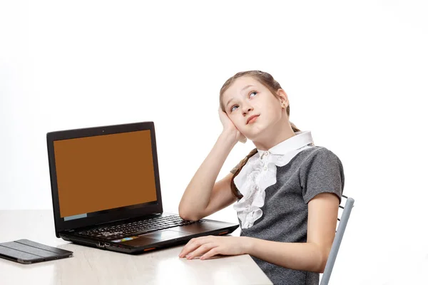 Schattig schoolmeisje zitten aan een laptop op een witte achtergrond — Stockfoto