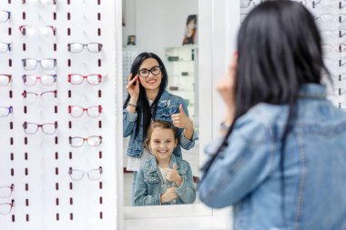 Optik mağazasında küçük güzel bir kız, annesiyle birlikte yeni gözlük seçiyor.