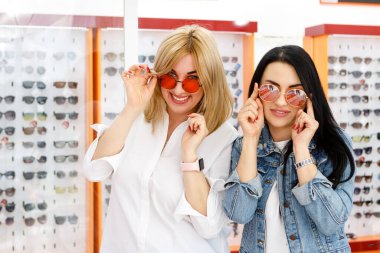 Optik mağazasında iki güzel kız yeni güneş gözlüğü seçiyor.