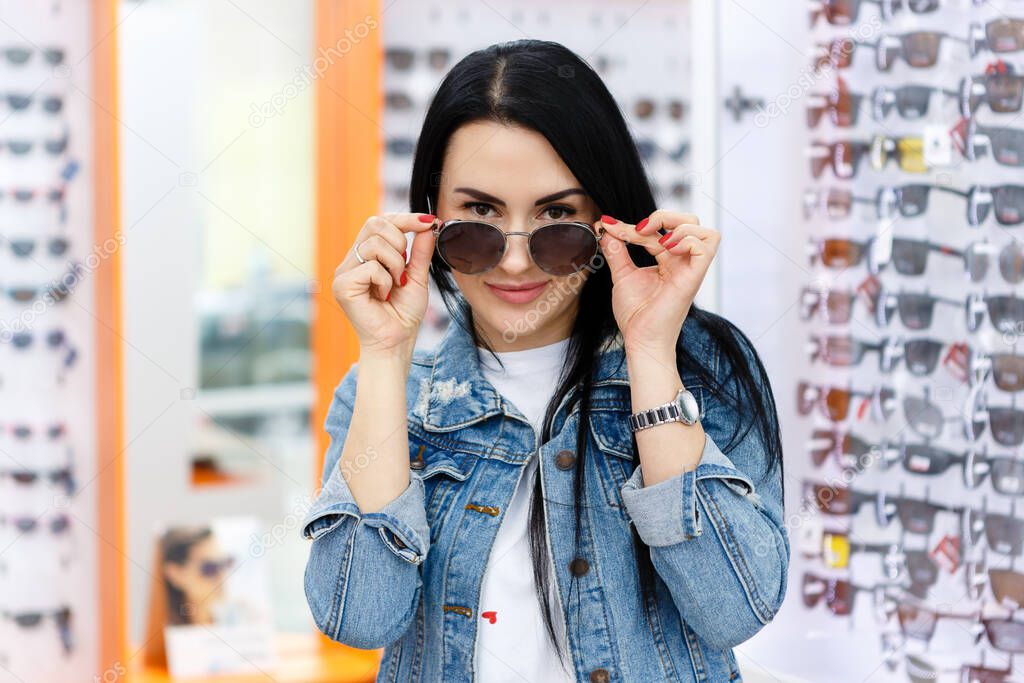 beautiful and fashionable girl in an optics store chooses new sunglasses