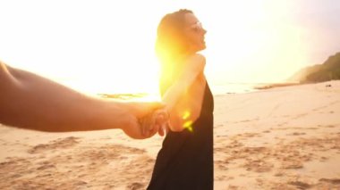 Genç bir çift boş sahilde günbatımı doğru yürüyen kadın önde gelen erkek arkadaş elele. seyahat kavramı