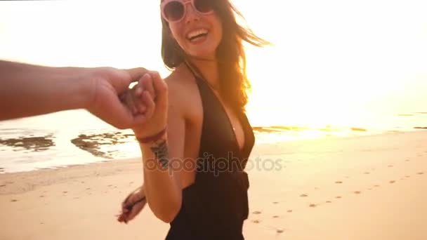 junges Paar Händchen haltend führt Frau Freunde in Richtung Sonnenuntergang am leeren Strand. Reisekonzept
