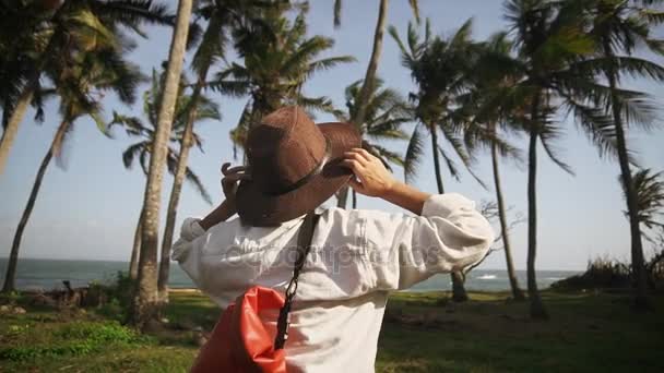 Молодая женщина с рюкзаком и шляпой среди кокосовых пальм радуется новым приключениям. Первооткрыватель. Время приключений . — стоковое видео