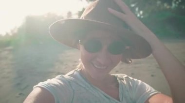 Genç bir kadın şapkası okyanus plaj gülümsüyor kamera üzerinde güneş ışığı altında yeni maceralar, tatil ve seyahat sahiptir. Palmiye ağaçları ile bir plaj arka plan üzerinde bir turist portresi