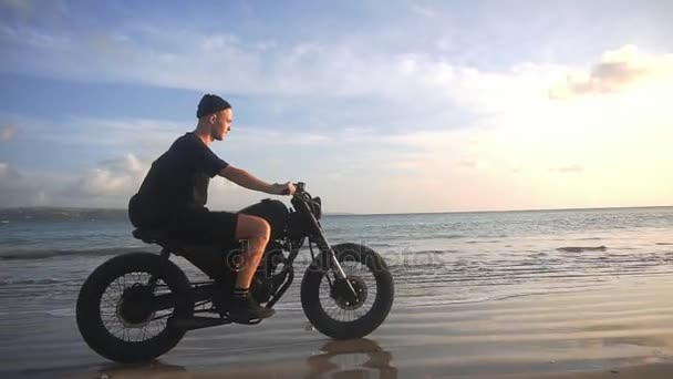 Мотоциклист ездит на мотоцикле по пляжу во время заката — стоковое видео