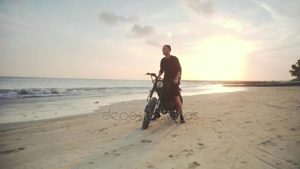 Motociclista dirigindo sua moto na praia durante o pôr do sol — Vídeo de Stock