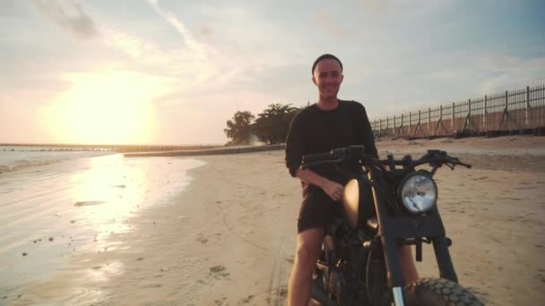 Motociclista dirigindo sua moto na praia durante o pôr do sol — Vídeo de Stock