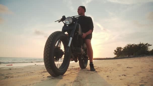 Motociclista dirigindo sua moto na praia durante o pôr do sol — Vídeo de Stock