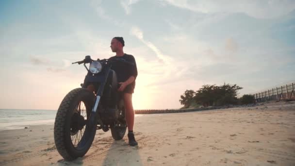 Motociclista conduciendo su moto en la playa al atardecer — Vídeos de Stock