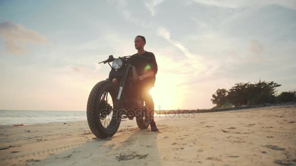 Motociclista conduciendo su moto en la playa al atardecer — Vídeos de Stock