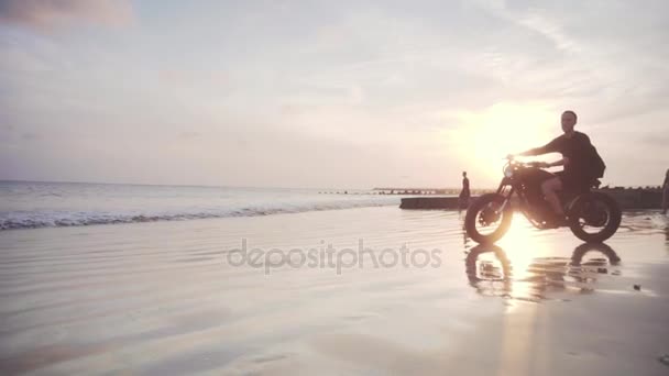 Motociclista che guida la sua moto sulla spiaggia durante il tramonto — Video Stock