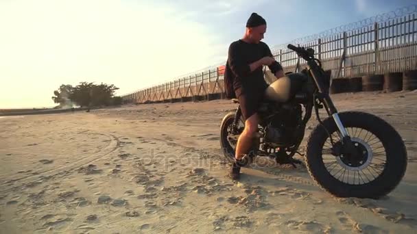 Motociclista conduciendo su moto en la playa durante el atardecer. Movimiento lento . — Vídeos de Stock