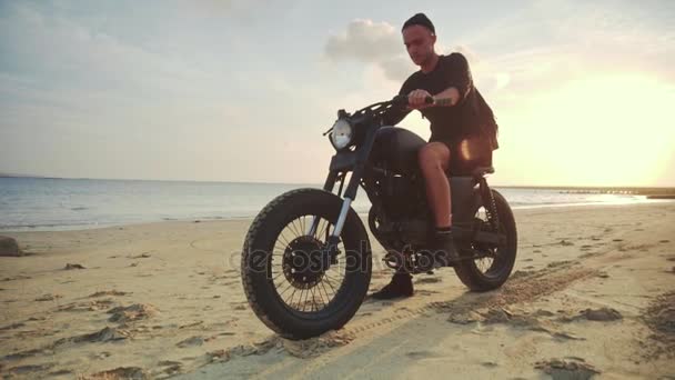 Motociclista conduciendo su moto en la playa durante el atardecer. Movimiento lento . — Vídeo de stock