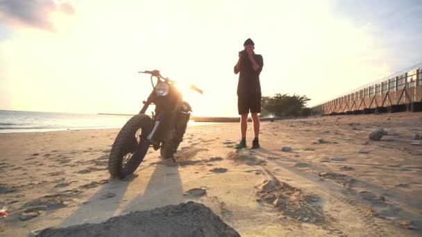 Motociclista atirando sua moto na praia durante o pôr do sol. Movimento lento . — Vídeo de Stock