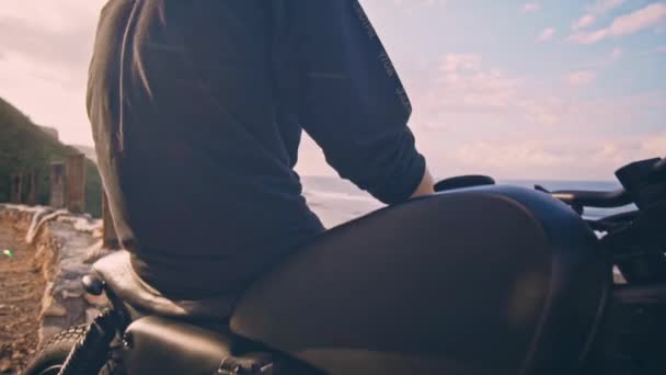 The motorcyclist sits on his motorcycle and admires a beautiful view of the mountains and the ocean, a halt on the way — Stock Video