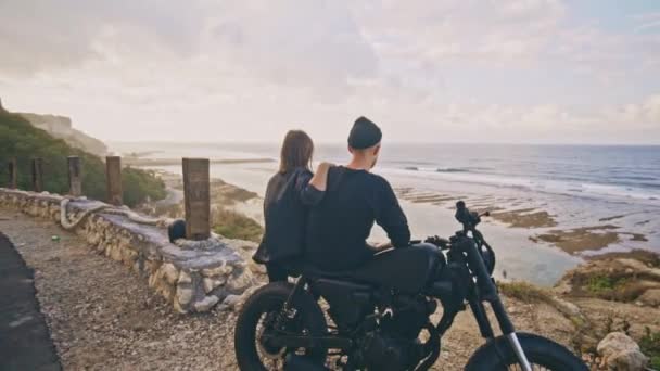 Een jonge vrouw met haar vriendje, de ruiter en zijn motorfiets bewonderen samen het prachtige uitzicht rondom, uitzicht op bergen en Oceaan — Stockvideo