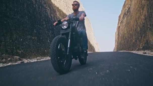 Motociclista dirigindo sua moto Entre duas pedras na praia do oceano — Vídeo de Stock