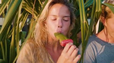 Gün batımında, arkalarındaki doğal dondurmalar yavaş evin çatısında bir palmiye ağacı yerken gülüyor birlikte neşeli bir ruh hali içinde iki kadın