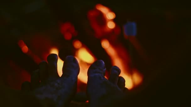 Homem que aquece os pés perto do fogo na praia ao pôr do sol — Vídeo de Stock