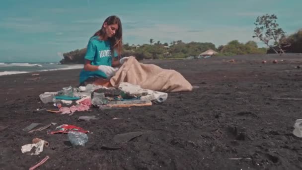 Volunteer sorting garbage on ocean beach, folding plastic bottles in an eco bag — Stock Video