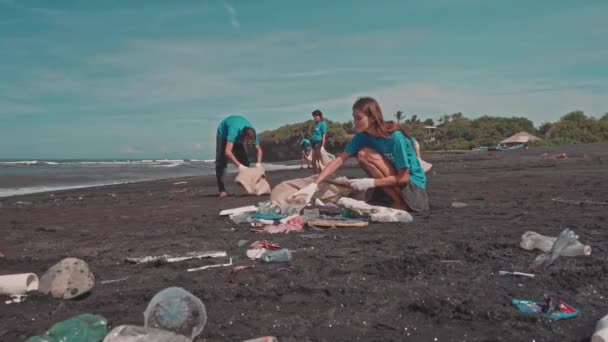 Добровольцы чистят пляж с помощью эко-мешка, сортируя пластик на пляже — стоковое видео
