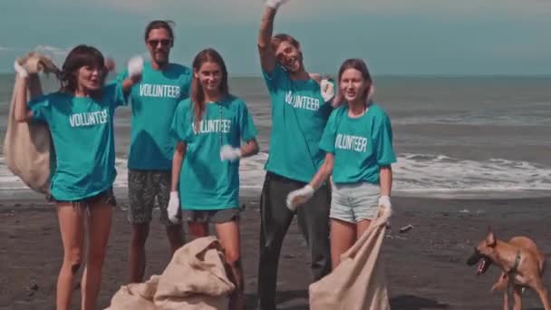 Vrijwilligers in blauwe ecologische t-shirts vieren overwinning op vuilnis op het strand — Stockvideo