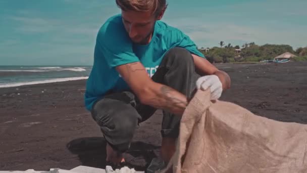 Vrijwilliger sorteren van afval op het strand van de oceaan, vouwen plastic flessen in eco tas — Stockvideo