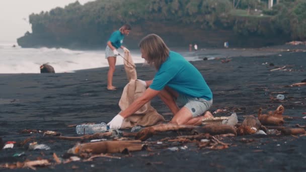 Zbliżenie wolontariuszy w niebieskiej koszulce, zbierających śmieci na plaży — Wideo stockowe