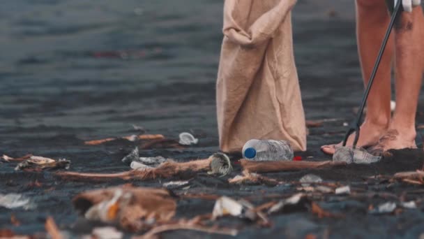 Man outdoors on the black sand beach gathering trash grabber stick — Stok Video