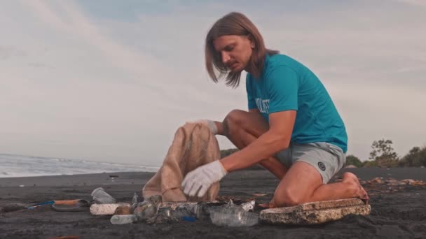 Camiseta voluntaria con zona de limpieza de bolsas ecológicas de basura en la playa de arena negra — Vídeo de stock