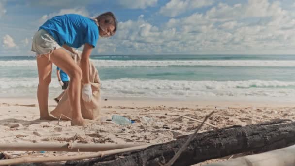 Dos voluntarios en camiseta azul recogiendo basura en bolsas ecológicas en la playa — Vídeo de stock