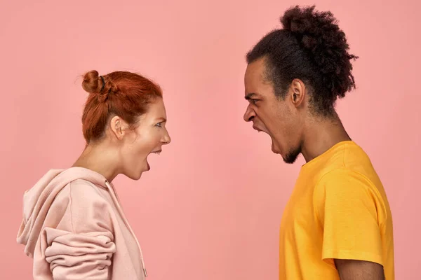 Furioso hombre negro enojado y mujer pelirroja tienen disputa, gritar en voz alta el uno al otro, disputa y resolver las relaciones, tienen desacuerdo, diferentes puntos de vista, se coloca sobre el fondo rosa . —  Fotos de Stock