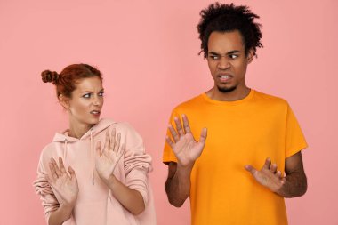 Hoşnut olmayan kızıl kız arkadaş ve koyu tenli erkek arkadaş ret jesti yapıyor, tiksiniyor, bir şey beğenmiyor, sıradan renkli kıyafetler giyiyor, pembe arka planda soyutlanıyor. Olumsuz duygular