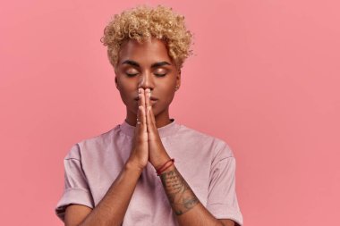 Minnettar, umut dolu genç siyahi kadın meditasyon pozisyonunda duruyor, huzurlu bir atmosferden hoşlanıyor, dua eden bir jestle el ele tutuşuyor, pembe arka planda izole edilmiş, iç huzur duygusu var. Meditasyon kavramı