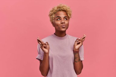 Şaşkın sarışın, esmer tenli kadın dua ederek dua ediyor, günlük yaz kıyafetleri giyiyor, pembe arka planda soyutlanıyor. Daha iyi olmak için büyük umut. İnsanlar ve vücut dili kavramı