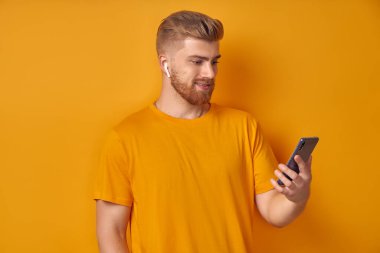 Beyaz sakallı yakışıklı adam gülümsüyor ve akıllı telefona bakıyor.