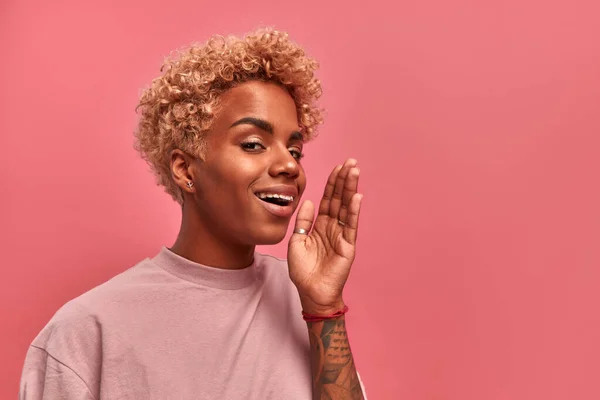 Hör upp. Närbild porträtt av glada unga afroamerikanska kvinna med blont hår håller hand nära hennes öppna mun och skrika om stor försäljning eller rabatter, på rosa bakgrund. Ansiktsuttryck — Stockfoto