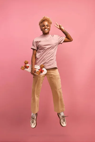 Full längd storlek skytte av afrikanska hoppa upp med skateboard på rosa vägg — Stockfoto