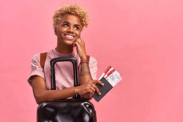 Happy pretty Afro vrouwelijke toerist met Bagage houdt paspoort en vliegtickets, blij met een tour in het buitenland met vriendje, heeft speciale aanbieding van reisbureau, op roze achtergrond — Stockfoto