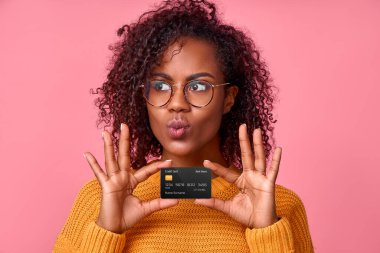 Güzel, Afro-Amerikan bir kadının portresi. Elinde banka kartı olan öpüşmeyi resmediyor. Pembe stüdyo arka planında online bir mağazadan bir şey alacak. Reklam için yer
