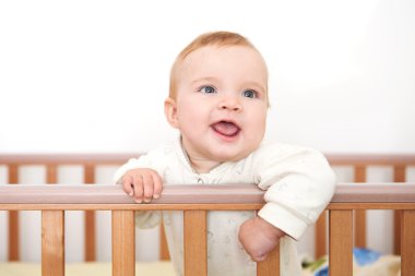 Bir bebek beşiğinde gülümsüyor ve yatağın tarafından tutar