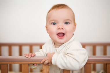 Bir bebek beşiğinde gülümsüyor ve yatağın tarafından tutar