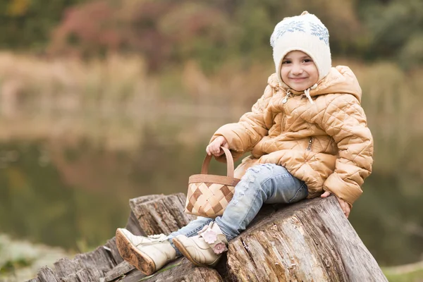 Entzückendes kleines Mädchen mit einem Korb am Ufer des Sees im Herbstpark — Stockfoto