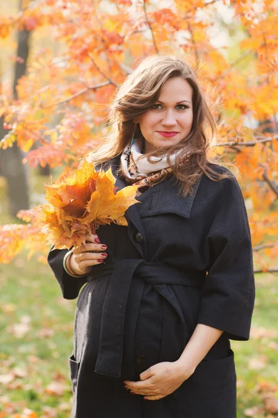 Mooie glimlachend zwangere vrouw staat in de herfst park — Stockfoto