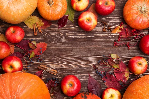 Thanksgiving background with apples, pumpkins and fallen leaves on wooden background. Autumn background