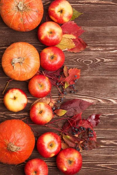 Thanksgiving background with apples, pumpkins and fallen leaves on wooden background. Autumn background