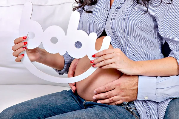 Belly of a pregnant woman , father and mother hands holding the word baby — Stockfoto