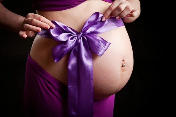 Belly of a pregnant woman in pink with a purple bow, newborn girl — Stock Photo, Image